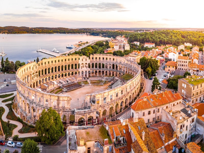 Das antike römische Amphitheater in Pula, Istrien, bei strahlendem Sonnenschein mit Blick auf die Arena und das Meer im Hintergrund.